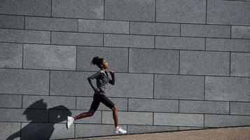 kant visie van jong Afrikaanse Amerikaans vrouw in sportief kleren dat loopt in de buurt muur foto