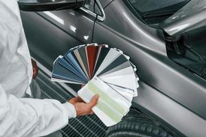 houdt kaarten met verschillend kleuren. Kaukasisch auto- klusjesman in uniform werken in garage foto