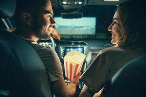 mooi gelukkig jong paar zittend in de auto samen en aan het eten popcorn foto