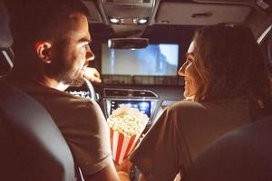 mooi gelukkig jong paar zittend in de auto samen en aan het eten popcorn foto