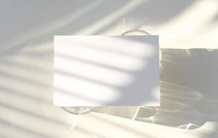 blanco bedrijf kaart mockup Aan glas met schaduw van natuurlijk bladeren schaduw bedekking Aan wit achtergrond, voor Product of presentatie foto