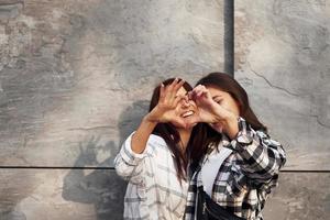 liefde gebaar. mooi vrolijk vrienden of lesbienne paar samen in de buurt muur buitenshuis Bij dag foto