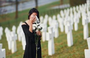 jong vrouw in zwart kleren bezoekende begraafplaats met veel wit kruisen. opvatting van begrafenis en dood foto