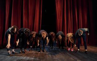 mensen buigen naar publiek. groep van acteurs in donker gekleurde kleren Aan repetitie in de theater foto