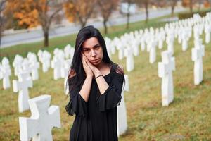 jong vrouw in zwart kleren bezoekende begraafplaats met veel wit kruisen. opvatting van begrafenis en dood foto