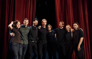 staand tegen rood gordijnen. groep van acteurs in donker gekleurde kleren Aan repetitie in de theater foto