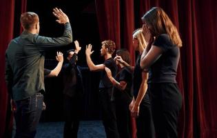 geven hoog vijf, vieren succes. groep van acteurs in donker gekleurde kleren Aan repetitie in de theater foto