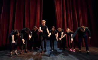 mensen buigen naar publiek. groep van acteurs in donker gekleurde kleren Aan repetitie in de theater foto