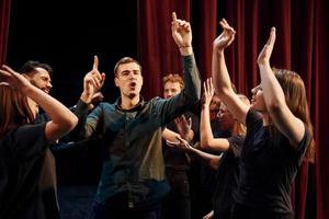 geven hoog vijf, vieren succes. groep van acteurs in donker gekleurde kleren Aan repetitie in de theater foto