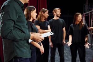 staand tegen rood gordijnen. groep van acteurs in donker gekleurde kleren Aan repetitie in de theater foto