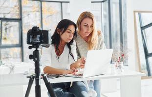 camera Aan statief is opname. twee jong vrouw freelancers werken binnenshuis in de kantoor met laptop foto