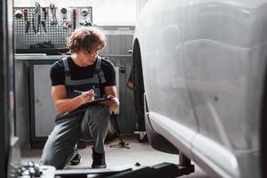 schrijven in kladblok. volwassen Mens in grijs gekleurde uniform werken in de auto- salon foto