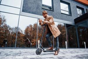 rijden elektrisch scooter. jong mannetje model- in modieus kleren is buitenshuis in de stad Bij dag foto