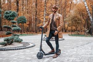 in de park Aan elektrisch scooter. jong mannetje model- in modieus kleren is buitenshuis in de park Bij dag foto