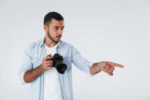 met professioneel camera. jong knap Mens staand binnenshuis tegen wit achtergrond foto