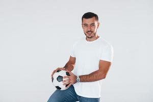 Amerikaans voetbal ventilator met voetbal bal. jong knap Mens staand binnenshuis tegen wit achtergrond foto