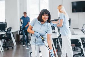 vrouw toepassingen vacuüm schoner. groep van arbeiders schoon modern kantoor samen Bij dag foto