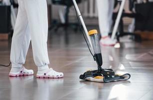 dichtbij omhoog visie van vrouw dat toepassingen vacuüm schoonmaakster binnen- in modern kantoor foto