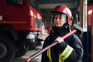 met hamer in handen. vrouw brandweerman in beschermend uniform staand in de buurt vrachtauto foto