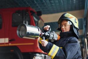 slang in handen. vrouw brandweerman in beschermend uniform staand in de buurt vrachtauto foto