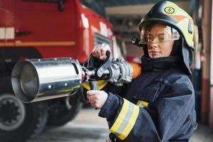 slang in handen. vrouw brandweerman in beschermend uniform staand in de buurt vrachtauto foto