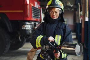 slang in handen. vrouw brandweerman in beschermend uniform staand in de buurt vrachtauto foto