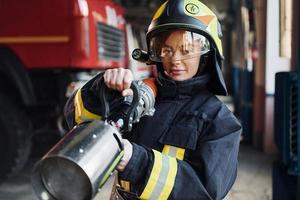 slang in handen. vrouw brandweerman in beschermend uniform staand in de buurt vrachtauto foto