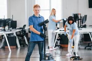 vent met vacuüm schoner. groep van arbeiders schoon modern kantoor samen Bij dag foto