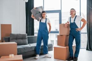 bezig dag. twee jong verhuizers in blauw uniform werken binnenshuis in de kamer foto