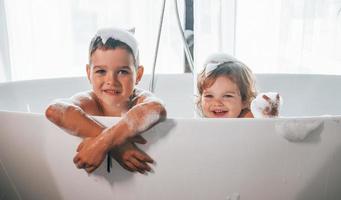 twee kinderen hebben pret en het wassen zich in de bad Bij huis. poseren voor een camera foto