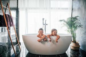 twee kinderen hebben pret en het wassen zich in de bad Bij huis. poseren voor een camera foto