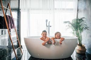 twee kinderen hebben pret en het wassen zich in de bad Bij huis. poseren voor een camera foto
