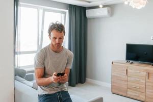 jong Mens in gewoontjes kleren is binnenshuis controlerend slim huis technologie foto