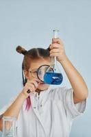 houdt vergroten glas. weinig meisje in jas spelen een wetenschapper in laboratorium door gebruik makend van uitrusting foto