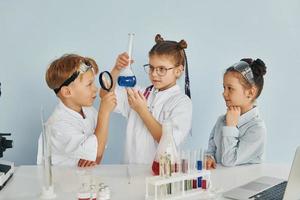 staand door de tafel met test buizen. kinderen in wit jassen Toneelstukken een wetenschappers in laboratorium door gebruik makend van uitrusting foto