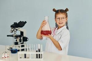 weinig meisje in jas spelen een wetenschapper in laboratorium door gebruik makend van uitrusting foto