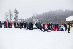 Minsk, Wit-Rusland, 16 februari 2022. mensen hebben pret Aan sneeuw buis. winter amusement.mensen staan in lijn naar glijbaan naar beneden de berg foto