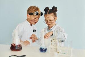 meisje met jongen werken samen. kinderen in wit jassen Toneelstukken een wetenschappers in laboratorium door gebruik makend van uitrusting foto