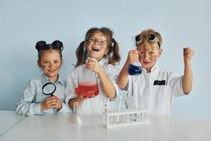 gelukkig vrienden lachend. kinderen in wit jassen Toneelstukken een wetenschappers in laboratorium door gebruik makend van uitrusting foto