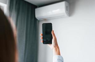 controlerend conditioner door tablet. jong vrouw is binnenshuis in kamer van modern huis Bij dag foto