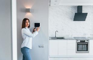 controlerend huis door een aanraken. jong vrouw is binnenshuis in slim huis kamer Bij dag foto