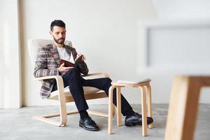 leest boek. jong elegant zakenman in pak binnenshuis. opvatting van succes foto