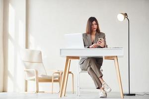 werken in de kantoor door laptop. jong vrouw in formeel kleren is binnenshuis. opvatting van stijl foto