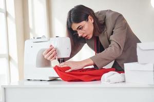 naaister werken met rood lap. jong vrouw in formeel kleren is binnenshuis. opvatting van stijl foto