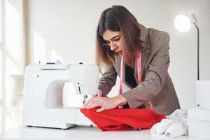 naaister werken met rood lap. jong vrouw in formeel kleren is binnenshuis. opvatting van stijl foto