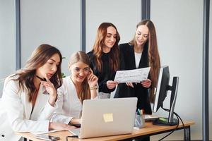 werken door tafel met laptop. groep van volwassen Dames dat in formeel kleren is binnenshuis in de kantoor samen foto