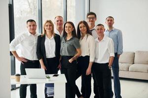 staand samen. groep van mensen in officieel formeel kleren dat is binnenshuis in de kantoor foto