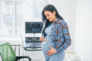 houdt resultaten van ultrasoon scannen. zwanger vrouw is in de kliniek in kabinet en hebben Gezondheid controleren foto