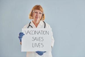 vaccinatie bespaart leeft spandoek. senior vrouw dokter in wit jas is staand binnenshuis foto