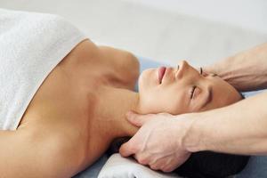 hoofd massage. jong vrouw is aan het liegen naar beneden wanneer Mens aan het doen procedure naar haar in spa foto